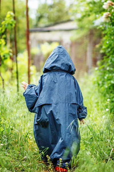 Funny little boy walks in the rain in a raincoat with a hood.