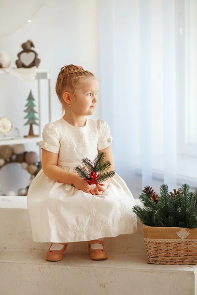 Portrait of a cute little blonde girl holding fir twig and looki