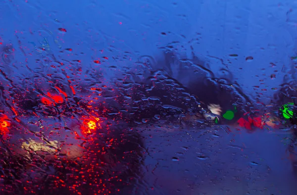 Blurry car silhouette seen through raindrops on the car windshie