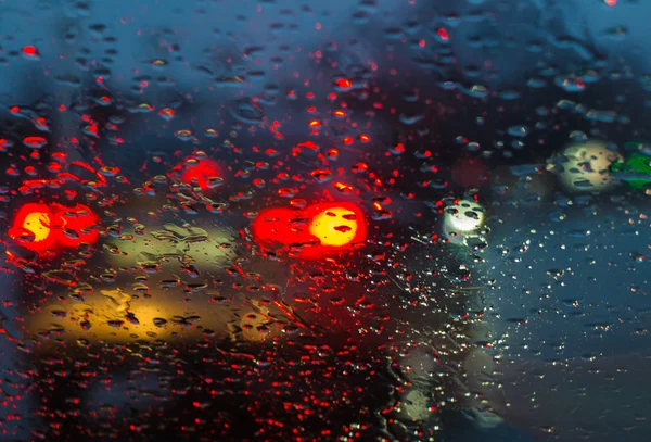 Blurry car silhouette seen through raindrops on the car windshie