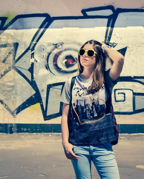 Stylish teenage girl in sunglasses posing near graffiti wall