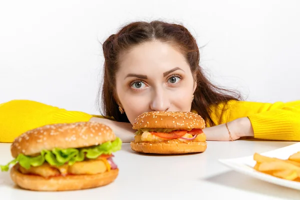Girl bites off a huge hamburger. Unhealthy diets.