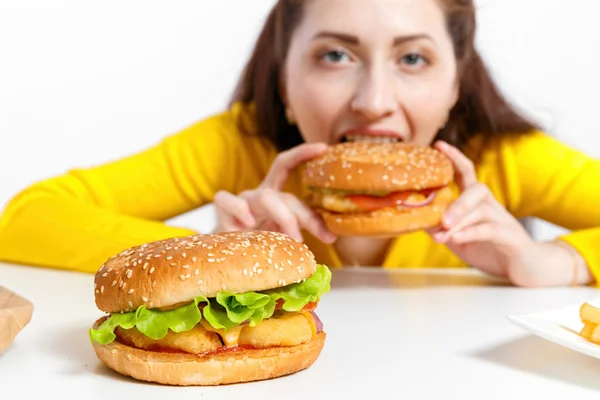 Girl bites off a huge hamburger. Unhealthy diets.