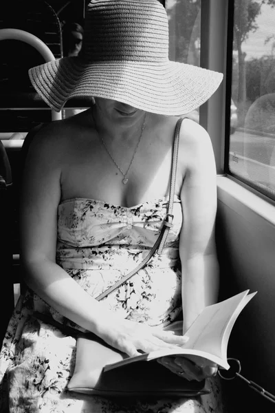 Woman in hat reading book on train bus