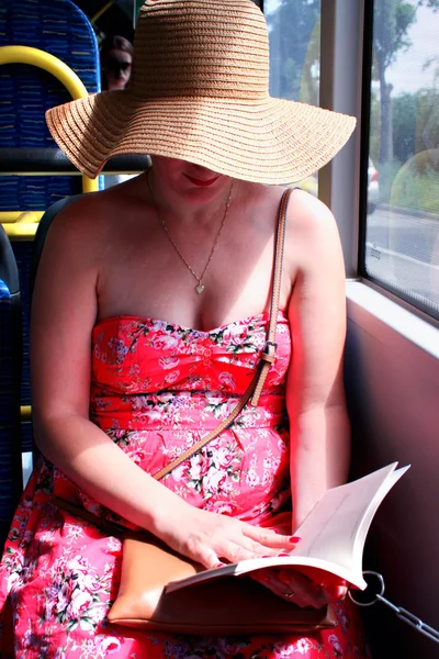 Woman in hat reading book on train bus