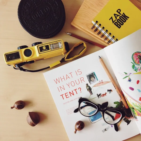 Yellow things out of my bag, an interesting opened book and note book, pens, glasses, yellow polaroid on the wooden table