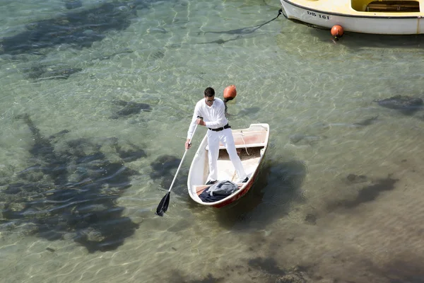 Man dressed in white standing in his dinghy using a paddle