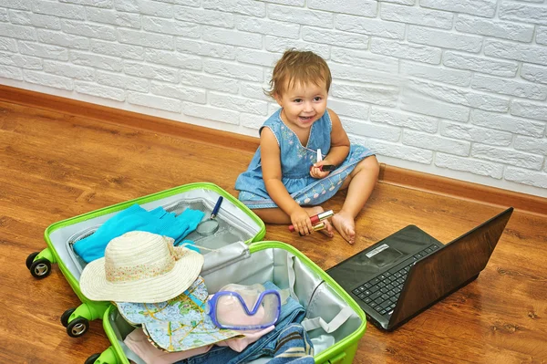 Little girl sitting on the floor near the suitcase and laptop .to prepare for the trip .