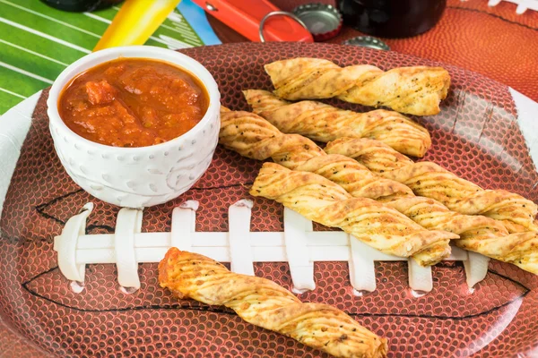 Plate with garlic cheese breadsticks on the table decorated for football game party.