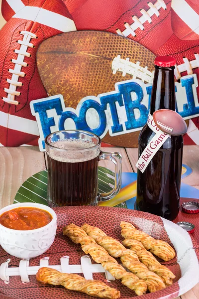 Glass of beer and plate with garlic cheese breadsticks on the table decorated for football game party.