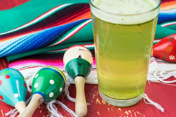 Glass of lime agua fresca, fiesta tradition wood maracas and colorful table runner.