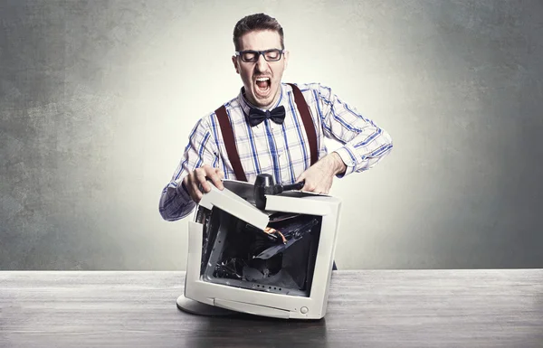 Young angry nerd destroying old computer monitor