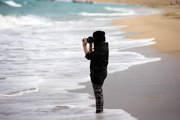 Arab woman photographer holding a dslr camera and taking a picture of the sea