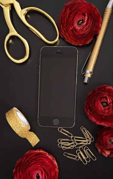 Red elegant flowers with phone and office accessories at black t