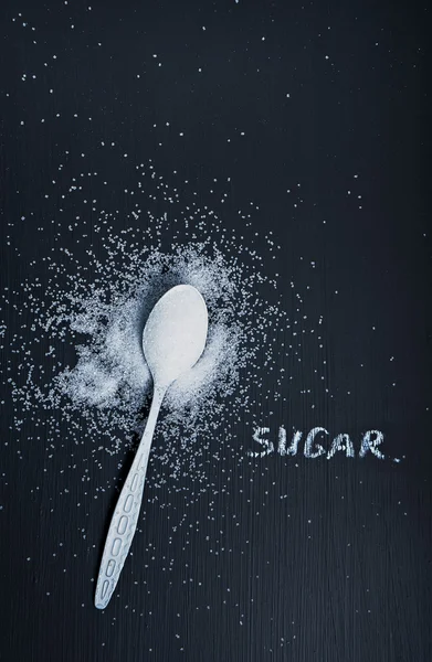 White sugar in white spoon on black table