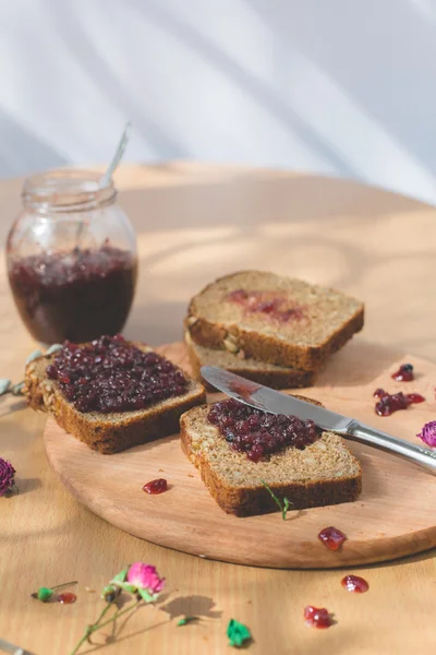 Fresh baked homemade healthy bread with blackcurrant jam - homemade marmalade with fresh organic fruits from garden. In rustic decoration, fruit jam on wooden table background. Perfect sweet breakfast