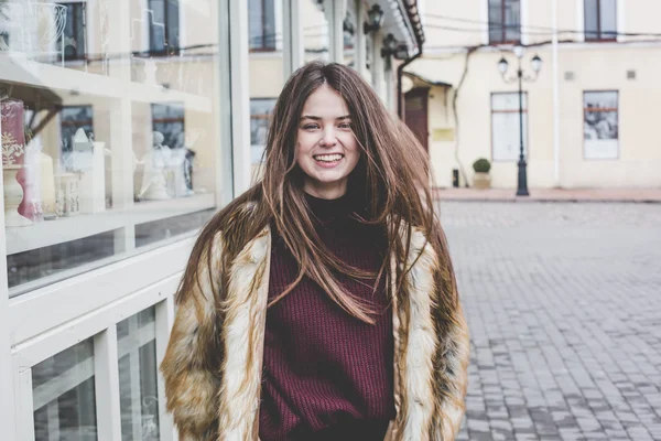Young hipster very beautiful caucasian stilysh and trendy girl with gorgeous brunette hair is having fun smiling outdoors on a background of the streets and wooden cool backgrounds during windy spring day