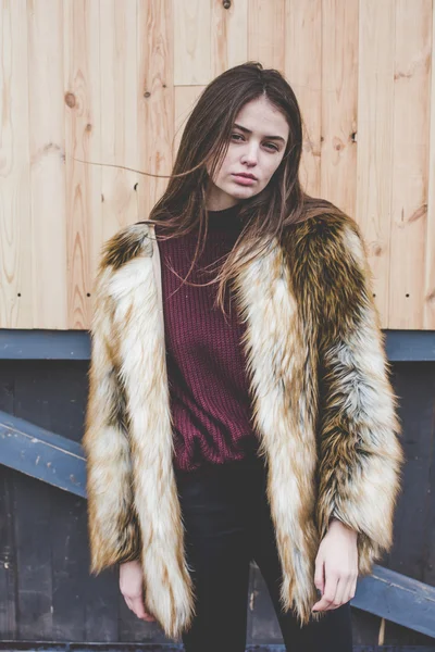 Young hipster very beautiful caucasian stilysh and trendy girl with gorgeous brunette hair is having fun smiling outdoors on a background of the streets and wooden cool backgrounds during windy spring day