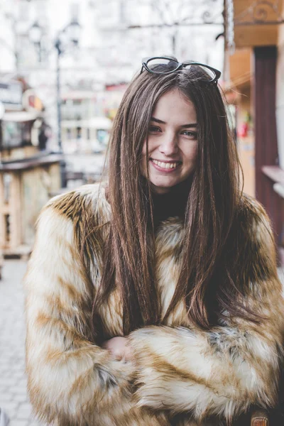 Young hipster very beautiful caucasian stilysh and trendy girl with gorgeous brunette hair is having fun smiling outdoors on a background of the streets and wooden cool backgrounds during windy spring day