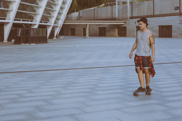 Cool young and handsome caucasian brunette hipster skater guy wearing a hat posing smiling and having fun outside while skating with his skateboard during amazing summer day in the city