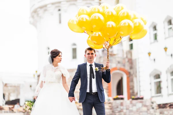 Young wedding couple walking outdoors with balloons