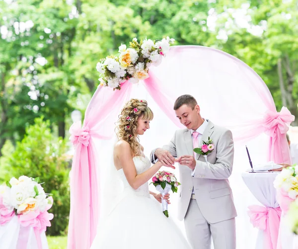 Groom putting a ring on brides finger during wedding ceremony