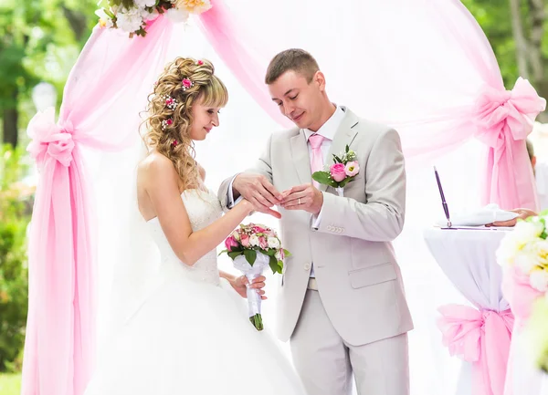 Groom putting a ring on brides finger during wedding ceremony