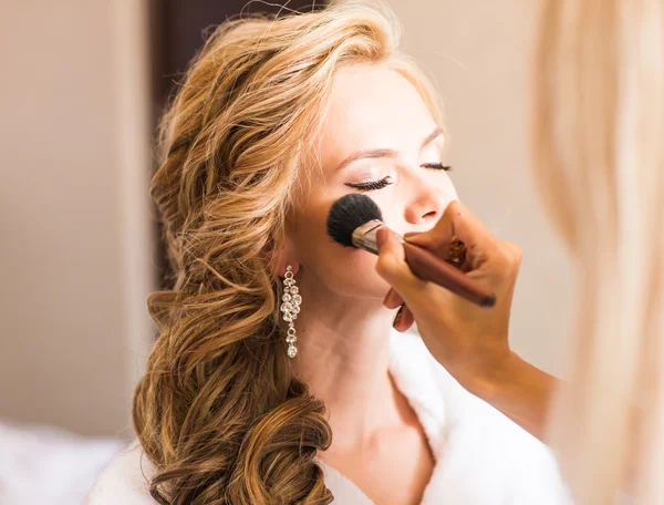 Wedding makeup artist making a make up for bride. Beautiful sexy model girl indoors. Beauty blonde woman with curly hair.  Close-up hands near face