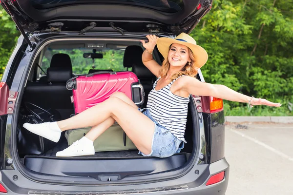 Cheerful woman on summer travel vacation sitting in a car trunk.