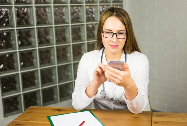 Female Medical Doctor Sitting at her Table and Browsing Something on Mobile Phone