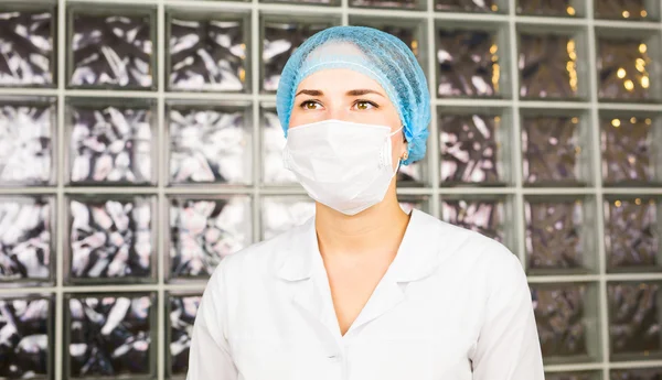 Young female scientist in surgical mask attentively looks in the modern laboratory