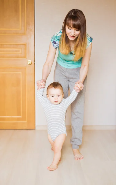 Mother teaching her cute little son to walk holding hands body part first baby steps concept