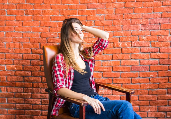 Beautiful smart woman sits on chair near brick wall
