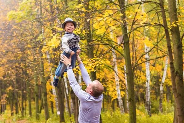 Father throws his happy laughing son in the air in the autumn park