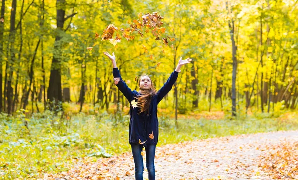 Happy girl  walks in autumn park throws up fallen maple leaves
