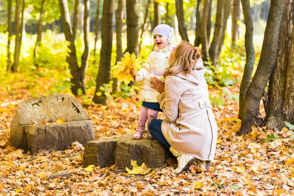 Mother kissing her daughter in the park.  Woman with child on autumn forest.