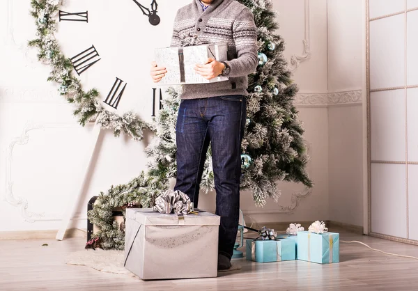 Young man holding gifts in front of Christmas tree