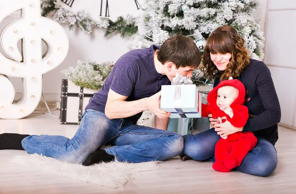 Christmas Family with baby opening gifts. Happy Smiling Parents and Child at Home Celebrating New Year