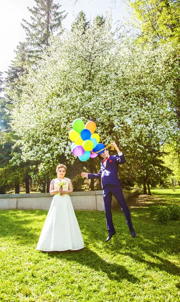 Groom flies on the balloons, but the bride holds his hand. Funny wedding. Groom jumps and flies on balloons. Young husband flying from his wife. Funny wedding concept. Happy Valentines day