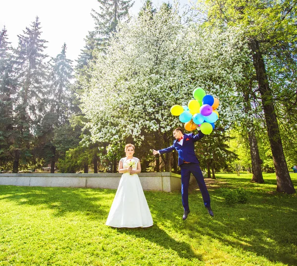 Groom flies on the balloons, but the bride holds his hand. Funny wedding. Groom jumps and flies on balloons. Young husband flying from his wife. Funny wedding concept. Happy Valentines day