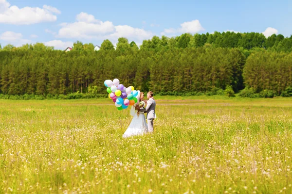 Beautiful bride holding bunch of balloons in the park. Couple of bride and groom with balloons. Newlyweds with balloons outdoors