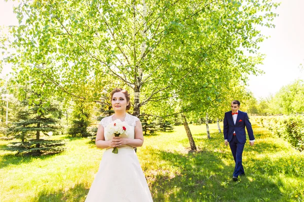 Couple in wedding attire with a bouquet of flowers and greenery is in the hands against the backdrop of the garden, the bride and groom