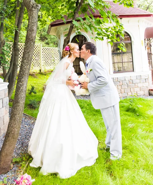 Couple in wedding attire with a bouquet of flowers and greenery is in the hands, the bride and groom kissing
