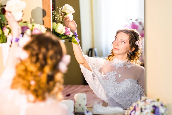 Beautiful bride in wedding dress with fan sitting in her bedroom near the mirror