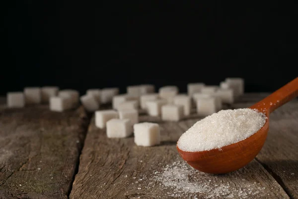 White sugar in a wooden spoon and sugar cubes