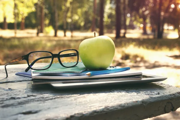 Stack notebook, apple and glasses on bench in a park