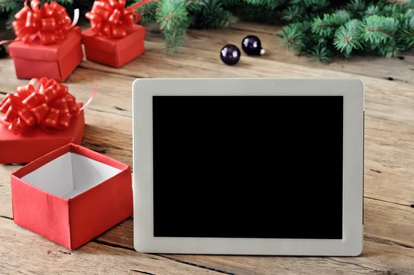White tablet computer with open Christmas gifts on wooden table
