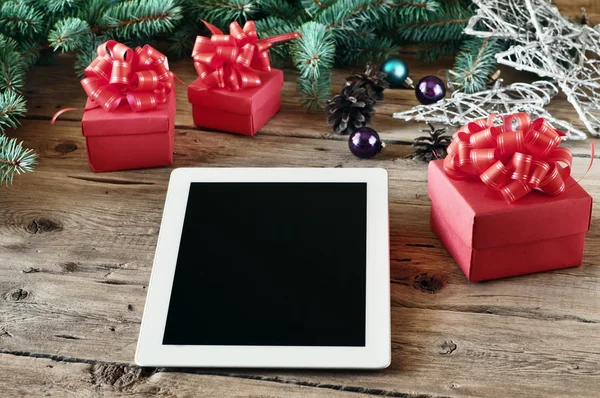 White tablet computer with Christmas gifts on wooden table close