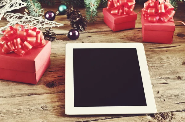 White tablet computer with Christmas gifts on wooden table close