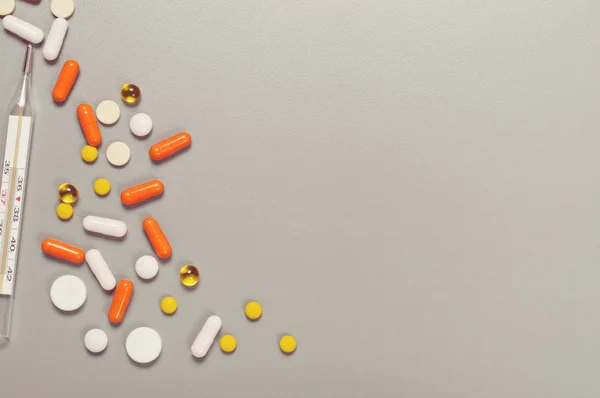 Scattered pills on a gray table with thermometer